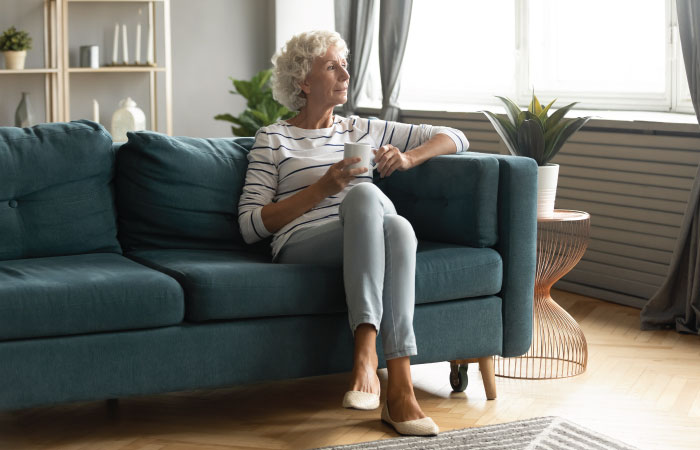 pensive older woman drinking coffee on a blue green couch